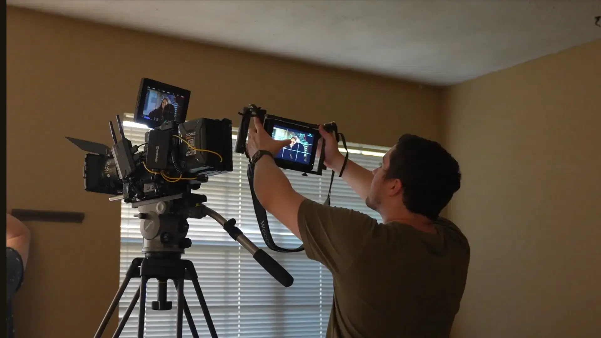 Crew member adjusts the framing of a professional cinema camera on a tripod while holding a handheld monitor