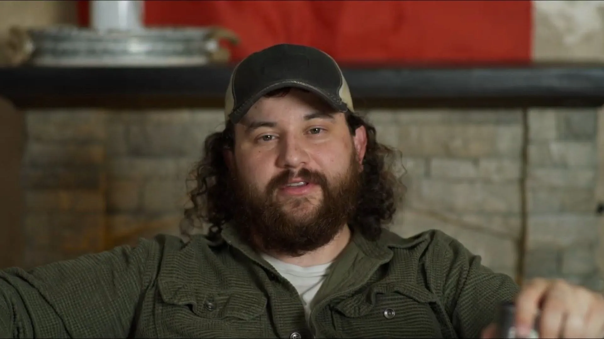 Bearded man in a cap and olive shirt answering an interview on set