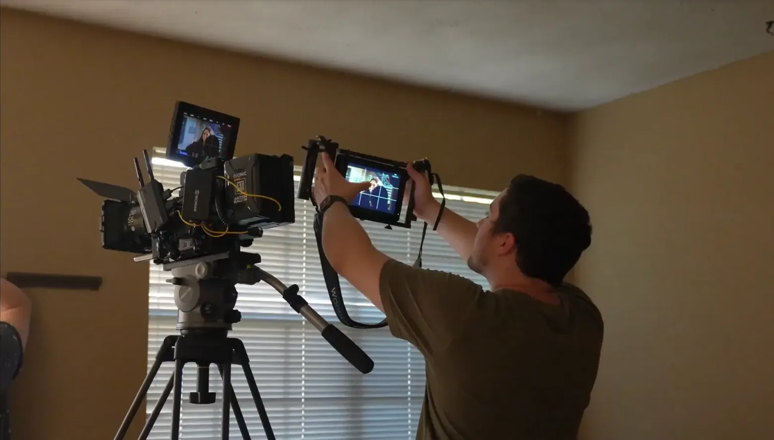 Cinematographer adjusting framing on a professional cinema camera mounted on a tripod in a warm interior